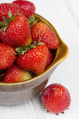 Fresh organic strawberries in bowl on white wooden background