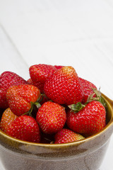 Fresh organic strawberries in bowl on white wooden background