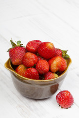 Fresh organic strawberries in bowl on white wooden background