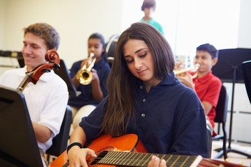 Female Pupil Playing Guitar In High School Orchestra © Monkey Business
