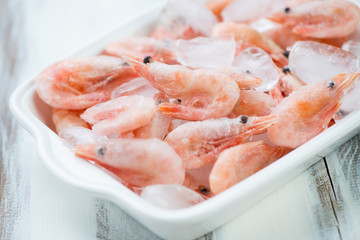 Glass bowl with raw frozen shrimps on ice cubes, horizontal shot