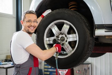 Cheerful serviceman unscrewing wheel in car workshop