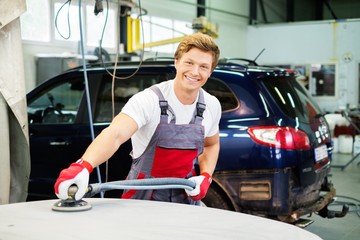 Serviceman performing grinding  on a car bonnet in a workshop