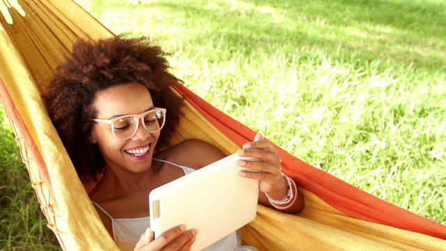laughing young woman in a hammock looking at digital tablet