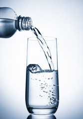 Pouring water into glass  from bottle on blue background