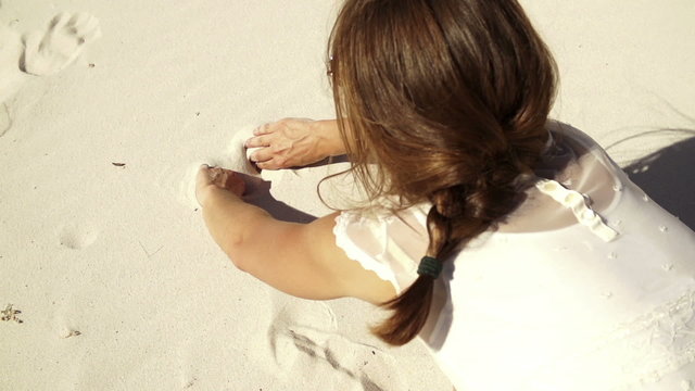 Girl is painting a heart into the sand