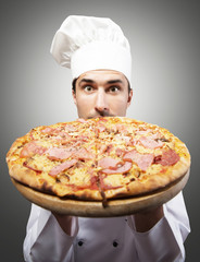 Humorous portrait of a man in chef's hat smelling pizza