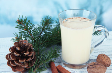 Cup of eggnog with fir branches on table on bright background