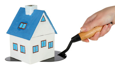 Hand holding wooden toy house on trowel, isolated on white