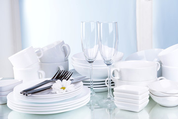 Set of white dishes on table on light background - obrazy, fototapety, plakaty