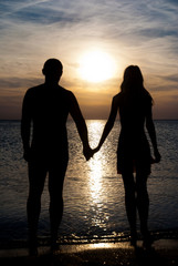 Young couple silhouette  on a sea beach holding hands and lookin