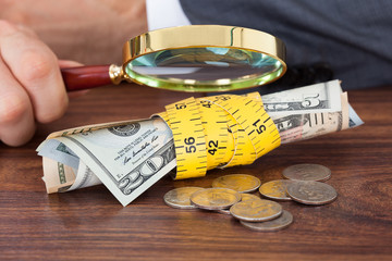 Businessman Examining Banknotes And Coins With Magnifying Glass
