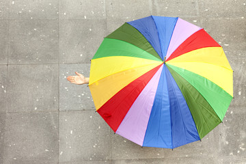 Woman hidden under multicolored umbrella and checking if it's ra