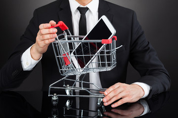 Businessman With Shopping Cart Model And Mobile Phone At Desk