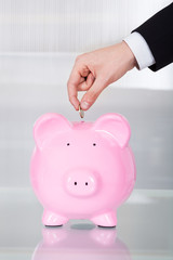 Businessman Inserting Coin In Piggybank In Office