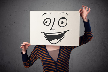 Woman holding a cardboard with smiley face on it in front of her