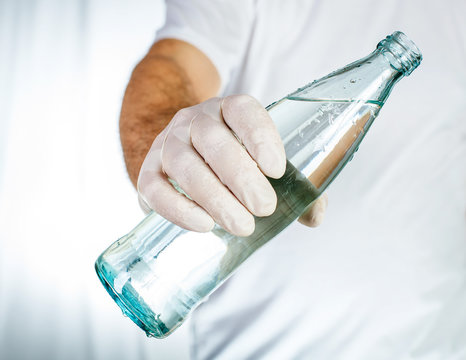 Male hand in latex glove holding glass bottle of water