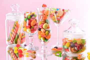 Different colorful fruit candy in glasses on pink background