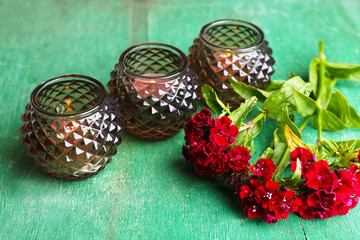 Glass candlesticks and flowers on color wooden background