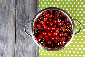 Sweet cherries in colander on color wooden background