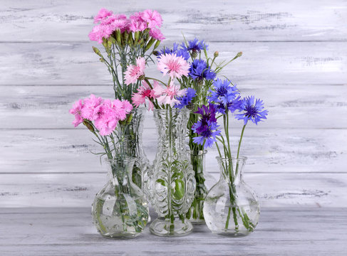 Beautiful summer flowers in vases on grey wooden background