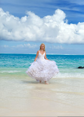 young beautiful woman in dress of bride runs on waves of sea