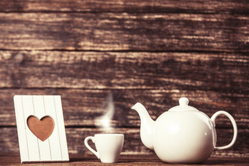 Teapot and cup of coffee with frame on wooden table.