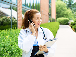 Fototapeta premium Portrait smiling female doctor on phone outdoors hospital campus