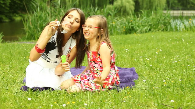 Mother with little daughter blowing a soap bubbles outdoor