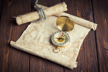 old unrolled map, rolled map and compass on wooden table