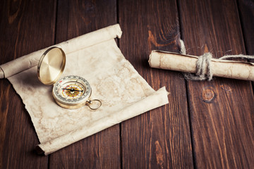old unrolled map, rolled map and compass on wooden table