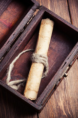 old paper roll inside treasure chest on wooden background