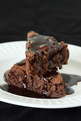 Slices of brownie on white plate covered with chocolate