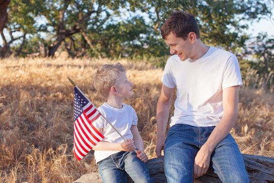 handsome father and his little son holding american flag celebra