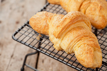 Fresh croissants on cooling rack on wooden background