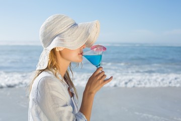 Smiling blonde relaxing by the sea sipping cocktail