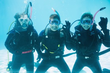 Friends on scuba training submerged in swimming pool making ok s