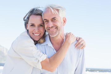Attractive couple hugging at the beach smiling at camera