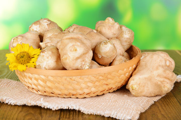 Topinambur roots in wicker basket on table on bright background