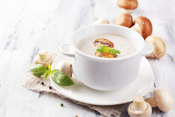 Mushroom soup in white pot, on napkin, on wooden background