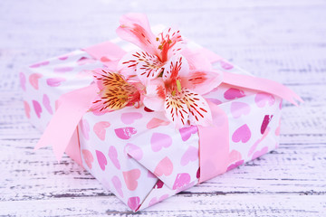 Pink gift with bow and flower on wooden table close-up