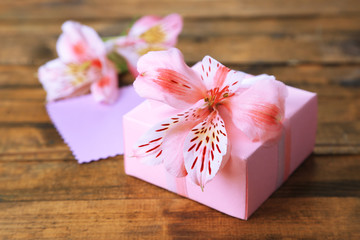 Pink gift with bow and flower on wooden table close-up