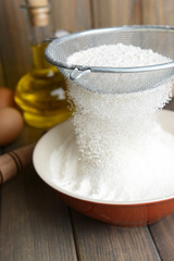Sifting flour into bowl on table on wooden background
