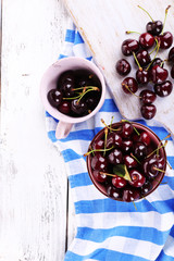 Sweet cherries in color bowl and mug on wooden background