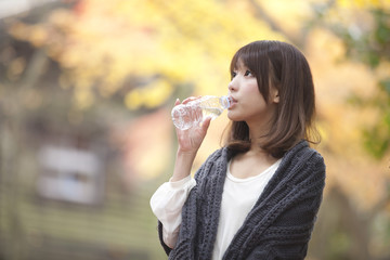 秋の紅葉した公園で立って水を飲んでいる女性