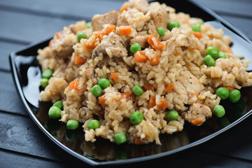 Chicken pilaf with green peas and carrot in a black glass plate