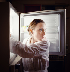 Fototapeta na wymiar Young woman looking for some snack in fridge late at night