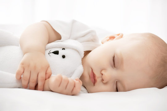 Carefree sleep little baby with a soft toy on the bed