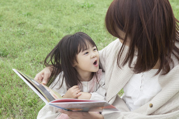 芝生で絵本を読む母と子