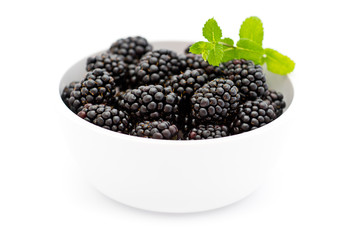 White bowl with pile of fresh blackberries and green mint